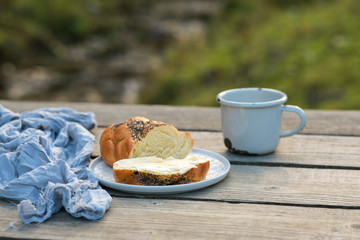 Scythe with poppy seeds, butter and tea. Baking with poppy seeds and coffee. The work of a baker. Poppy seed baking and pies.Bakery, cook together. Bun with butter on the nature in the forest. Picnic