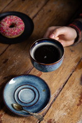 Tasty strawberry sprinkled donut, vintage tea spoon, black americano coffee in blue cup in male hand. Concept breakfast in coffee house. Vertical