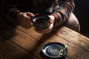 Closeup black americano coffee in blue cup in male hand, saucer with vintage tea spoon on...