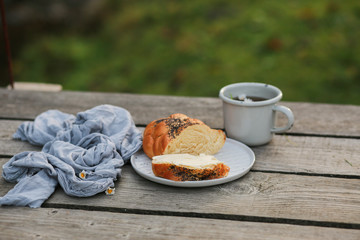 Scythe with poppy seeds, butter and tea. Baking with poppy seeds and coffee. The work of a baker. Poppy seed baking and pies.Bakery, cook together. Bun with butter on the nature in the forest. Picnic