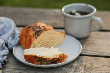 Scythe with poppy seeds, butter and tea. Baking with poppy seeds and coffee. The work of a baker. Poppy seed baking and pies.Bakery, cook together. Bun with butter on the nature in the forest. Picnic