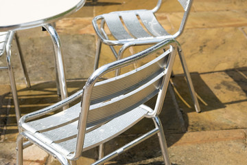 Metal street furniture at an outside cafe seen after a heavy downpour. The wet pavement which is slippery is visible in the background. Customers ran in for cover.