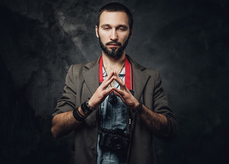 Portrait of calm bearded reporter with photo camera on the dark background.