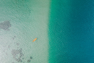 Top down aerial view of orange kayak with two woman on turquoise water at shallow sea shore. Kayaking during summer vacation. High angle background with copy space. Primorsky Krai, Far East, Russia