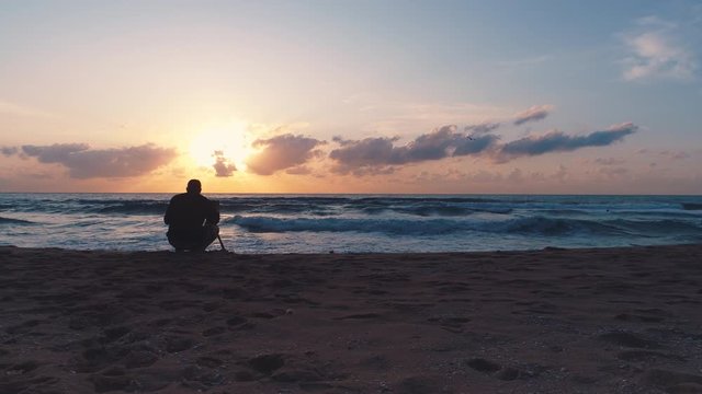 Photographer taking photos of sea and dramatic sunrise on the beach