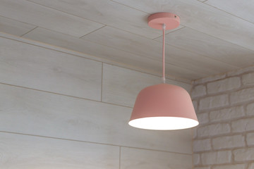 A pink electric lamp with the lights turned on hangs from the ceiling against the background of the...