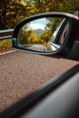 VVertical view of a mountain peak and  forest in autumn from the rearview mirror of a car on the road. 