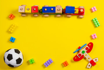 Kids toys background. Wooden train, plane, soft soccer ball and colorful blocks on yellow background