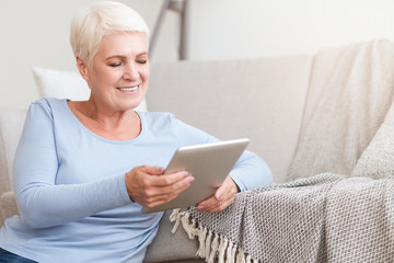 Happy old woman using digital tablet at home