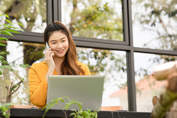 Fototapeta premium Business Asian young woman working with laptop smile and talking with customer in smartphone to get idea and requirement for success job outside office in coffee shop,Small Business Startup Concept
