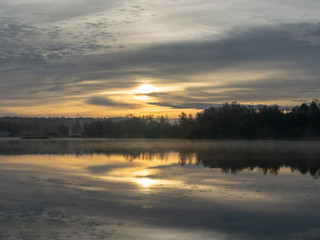 early autumn morning, white mist over water and ground, beautifully colored and blurred tree silhouettes in the background