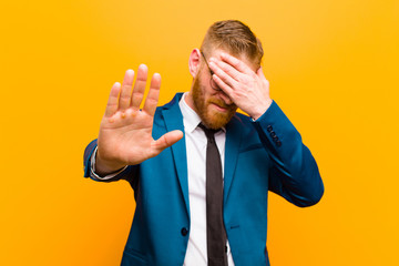 young red head businessman covering face with hand and putting other hand up front to stop camera,...