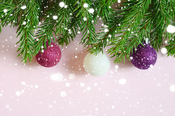 Fototapeta na wymiar christmas tree branches with christmas decorations toys balls, frame on a pink background. falling snow