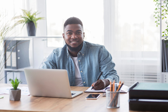 Portrait of smiling black trainee taking notes at new workplace
