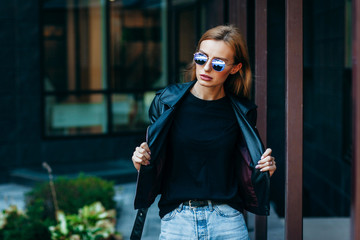 Girl wearing t-shirt, glasses and leather jacket posing against street , urban clothing style....