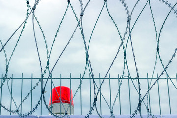 fence with barbed wire and a signal red lamp against a cloudy sky