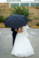 Bride and groom at wedding Day walking Outdoors. Bridal couple, Happy Newlywed woman and man under umbrella. Loving wedding closeup.