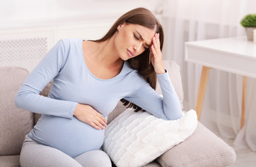 Pregnant Woman Suffering From Migraine Sitting On Couch At Home
