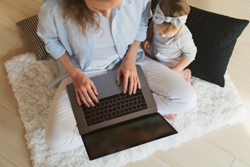View from above. Baby girl sitting on floor with mother. Woman holding laptop on her knees and...