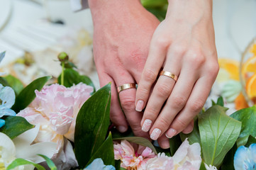 A pair of gold wedding rings on a bride's and groom's hands. Closeup.