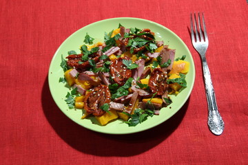 Salad of baked pumpkin, jerked tomato, meat, parsley, sesame, oil, balsamic on green plate onred  cover 