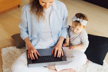 Obraz premium Mother and little daughter sitting on floor and watching videos for kids. Distant work for young parents in digital segment.