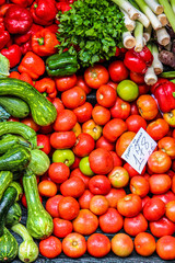 Fresh vegetables on the farmers market. Handwritten paper in Portuguese with names of the vegetable sort and price. Organic food. Red tomatoes, green zucchinis, red peppers, leek. Vegetarian cooking