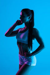 Fototapeta na wymiar Young sportswoman with perfect body isolated on blue light background