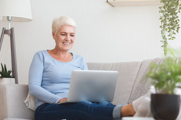 Smiling old woman typing email on laptop