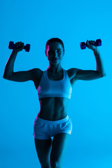 Fototapeta na wymiar Fitness young woman working out with dumbbells isolated on blue light background