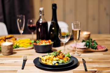 Festive table setting. Food and drinks, plates and glasses. Evening lights and candles. New Year's Eve.