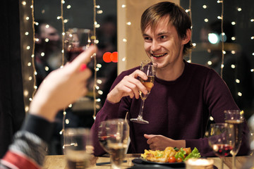 Friends holiday party dinner at home around the table. Celebrate Christmas. People eat, drink champagne, talk and laugh.