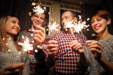 A group of friends, men and women, celebrate Christmas. Burning sparklers.