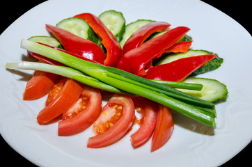 vegetable slices on a black background. Tomatoes, cucumbers, peppers, green onions.