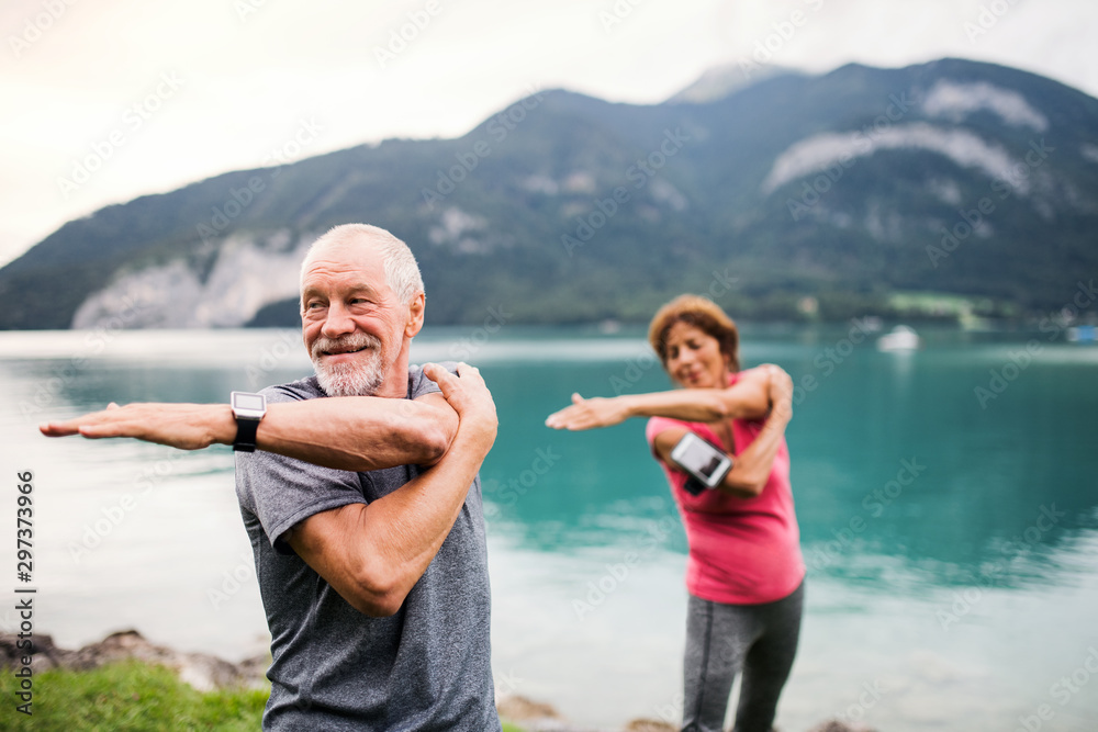 Sticker senior pensioner couple with smartphone by lake in nature, doing exercise.