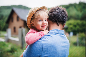 A close-up of father with toddler boy standing outdoors in garden in summer.