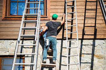 A father and toddler boy outdoors in summer, painting wooden house. © Halfpoint
