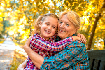 Fototapeta premium Smiling grandmother and granddaughter hugging and smiling in autumn park