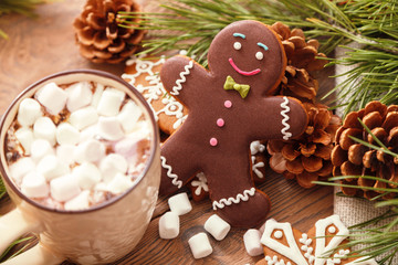 Gingerbread man and hot chocolate with marshmallows, on the background of Christmas tree branches on a wooden table
