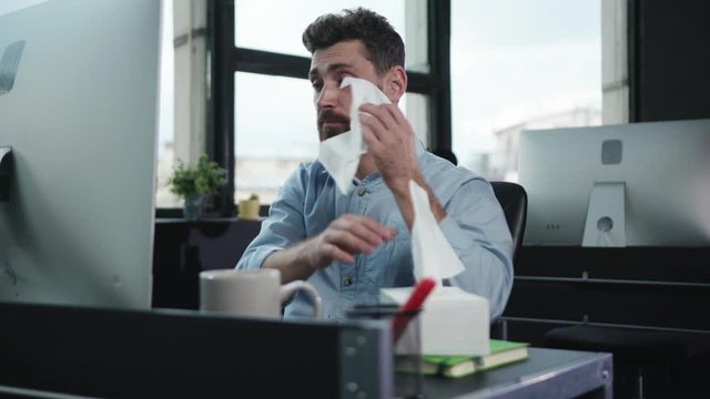Tired sick business manager working at desktop computer sneezing allergy blowing nose suffering virus cold. Office people. Bad condition.