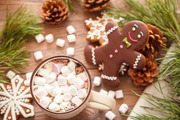Gingerbread man and hot chocolate with marshmallows, on the background of Christmas tree branches on a wooden table
