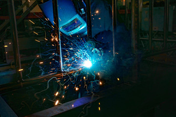 Fototapeta na wymiar A welder at work in a workshop produces metal structures. Sparks from welding fly around.