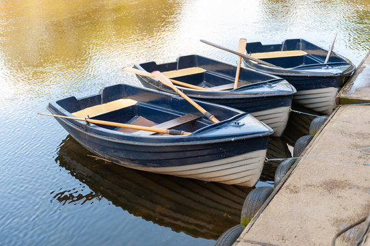 Close up of three blue and white rowing boats moored on a tranquil river on a sunny day