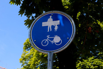 Pedestrian and bicycle shared road sign, blue circle traffic sign against trees and blue sky Road sign pedestrian priority in a street of  Zurich