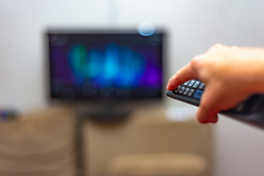 A man presses the red power button on the remote control to turn off the TV.