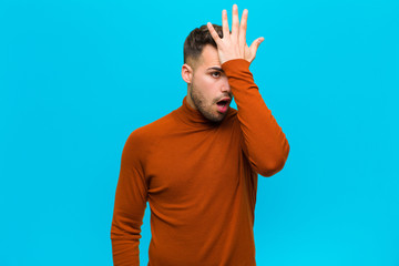 young hispanic man raising palm to forehead thinking oops, after making a stupid mistake or...