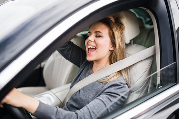 Cheerful young woman driver sitting in car, driving.