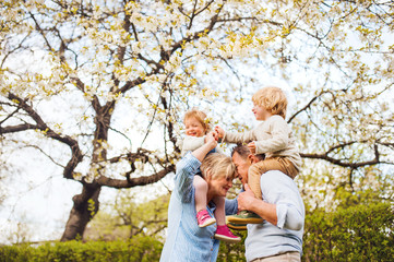 Senior grandparents with grandchildren standing under tree in blossom in spring.
