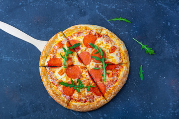 A fresh prepared pepperoni pizza with salami, tomatoes and cheese on a dark background. Italian traditional lunch or dinner. Fast food and street food concept. Flat ly, top view,