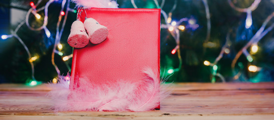 A big Christmas wish book with Xmas tree toys and decorations on wooden table. A read leather notepad - a gift for Christmas or New year